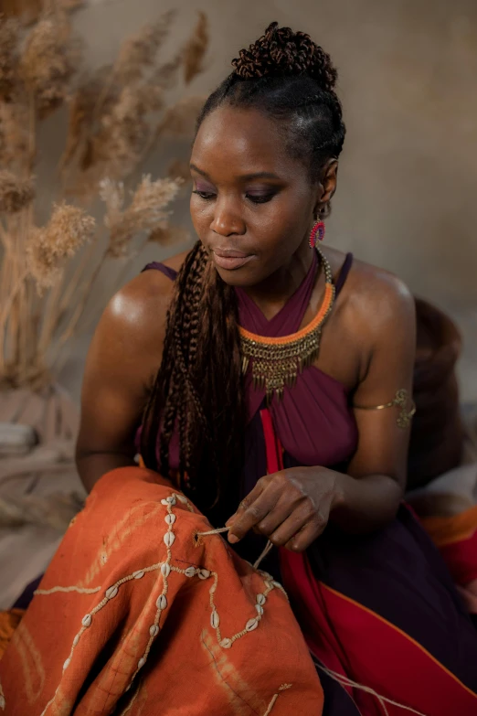 a woman sitting on the ground working on a piece of cloth, a portrait, inspired by Afewerk Tekle, trending on unsplash, wearing a dress made of beads, woman with braided brown hair, production photo, wakanda