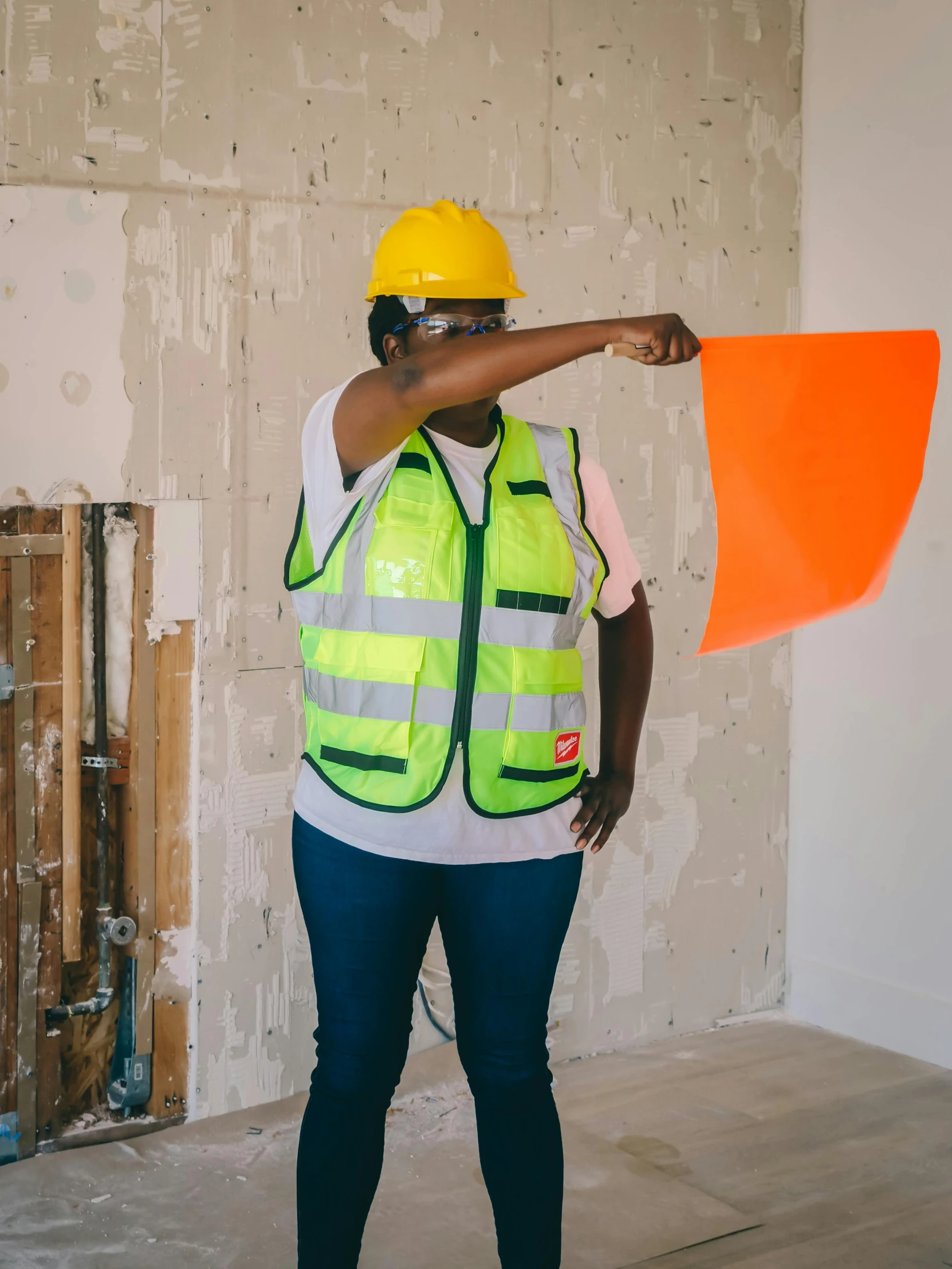 a woman in a hard hat holding an orange flag, a photo, by Arabella Rankin, pexels contest winner, arbeitsrat für kunst, bullet proof vest, neon-yellow-holographic wings, thicc build, woman holding sign