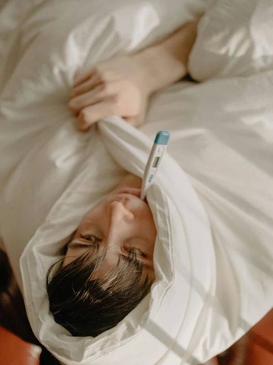 a person laying in bed with a toothbrush in their mouth, trending on pexels, happening, cloak covering face, wearing white cloths, ignant, holding a syringe