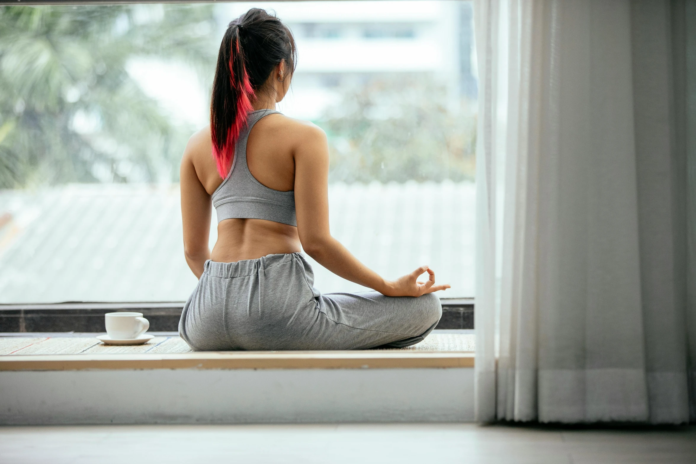 a woman sitting on a window sill doing yoga, a picture, inspired by Kanō Tan'yū, trending on pexels, exposed midriff, in a gym, manuka, from the back