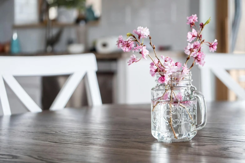 a vase filled with pink flowers sitting on top of a wooden table, pexels contest winner, kitchen table, sakura trees, glass jar, background image