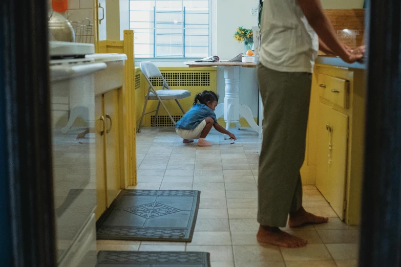 a woman standing in a kitchen next to a child, a picture, unsplash, yellow carpeted, movie scene, ignant, people at work