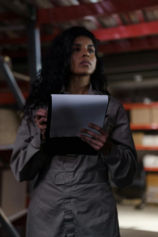 a woman standing in a warehouse holding a tablet computer, pexels contest winner, serial art, confidential documents, female with long black hair, movie scene close up, promotional image