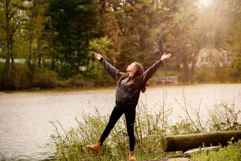 a woman standing in front of a body of water, being delighted and cheerful, soaring over a lake in forest, sun overhead, promo image