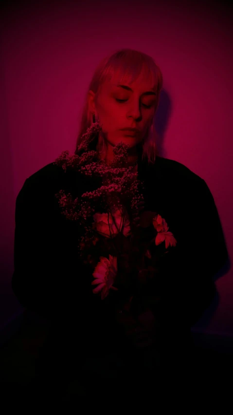 a woman standing in front of a pink wall, an album cover, inspired by Elsa Bleda, pexels, dark flowers, lit from below with red lighting, profile image, a blond