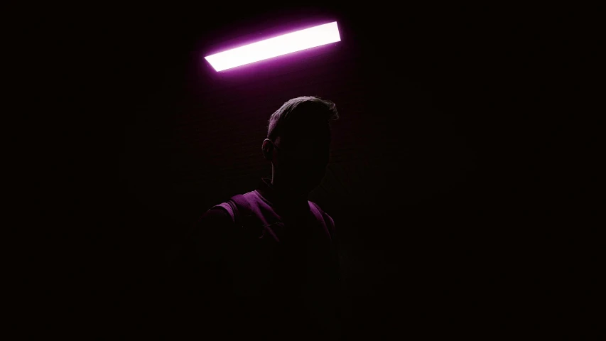 a man standing under a neon light in the dark, an album cover, unsplash, light and space, pink violet light, ceiling hides in the dark, 8k selfie photograph, with a black background