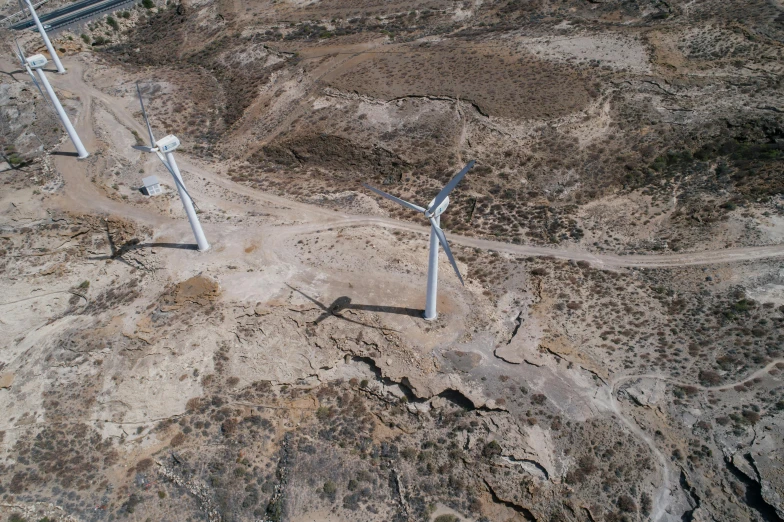 a couple of wind turbines sitting on top of a dirt field, unsplash, les nabis, “ aerial view of a mountain, cyprus, crashed, drone photo