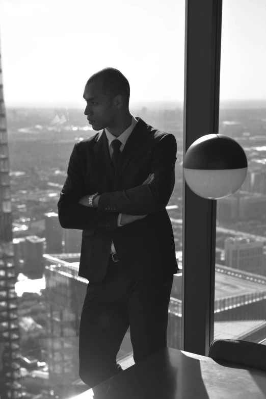 a man in a suit standing in front of a window, an album cover, unsplash, jayson tatum, bw, skyscapers, nathan for you