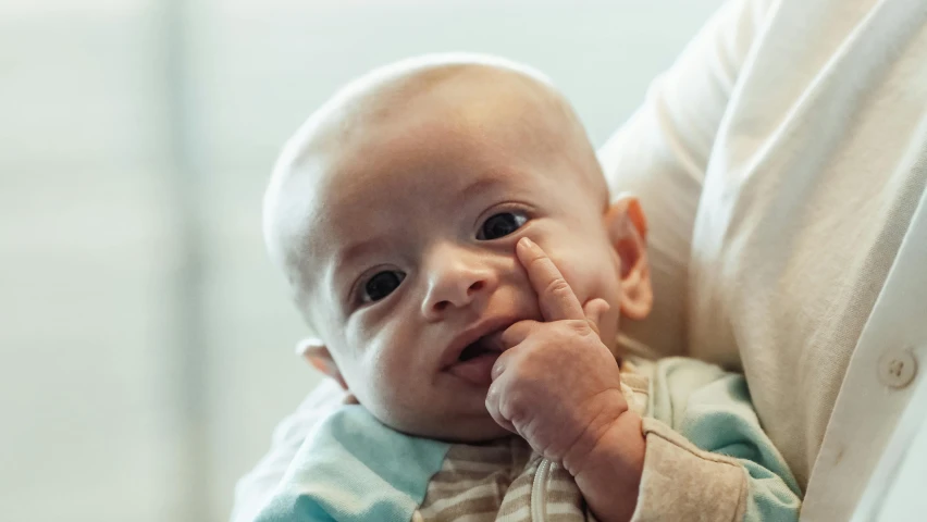 a close up of a person holding a baby, unsplash, photorealism, hand on his cheek, with pointing finger, focused expression, screensaver