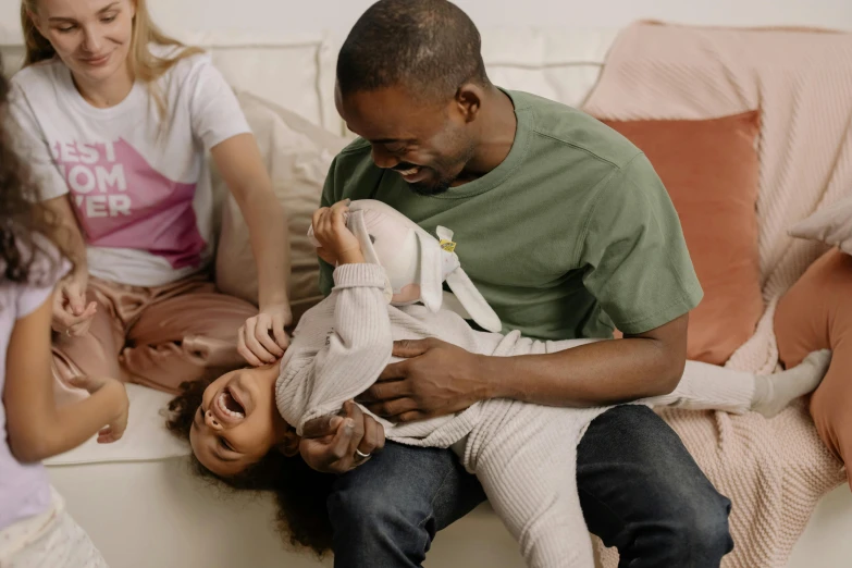 a man sitting on top of a couch holding a baby, pexels contest winner, kids playing, wearing a tee shirt and combats, daughter, green and brown clothes