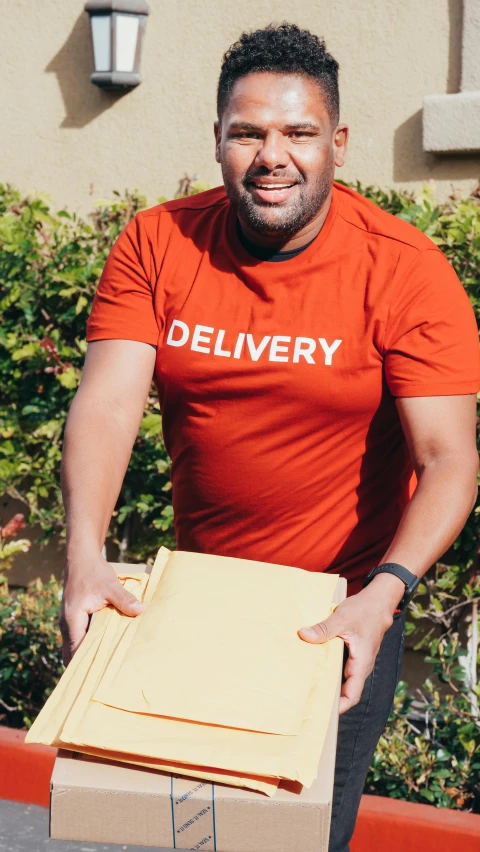 a man in an orange shirt holding a box, pexels contest winner, hurufiyya, logo for lunch delivery, wearing a t-shirt, hand on hips, ( ( dark skin ) )