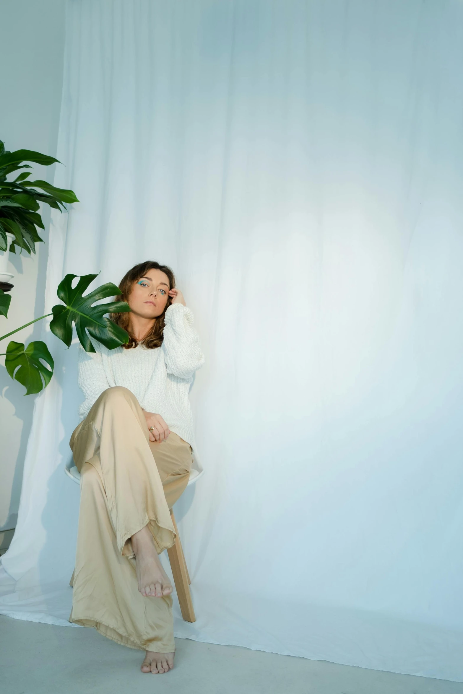 a woman sitting on a chair next to a potted plant, wearing a white sweater, non-illuminated backdrop, cynthwave, fully covered in drapes