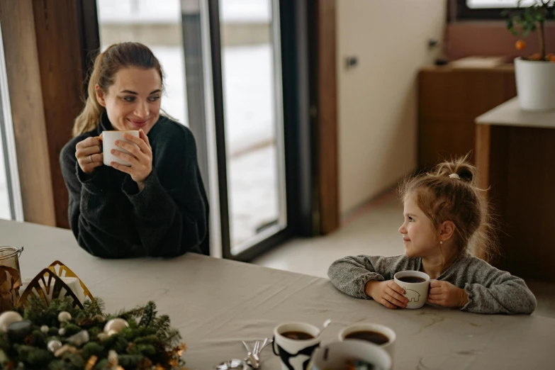 a woman and a little girl sitting at a table, by Emma Andijewska, pexels contest winner, hot cocoa drink, manuka, calmly conversing 8k, slightly minimal