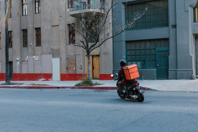 a man riding on the back of a motorcycle down a street, by Tom Bonson, pexels contest winner, postminimalism, getting groceries, square, los angeles ca, orange