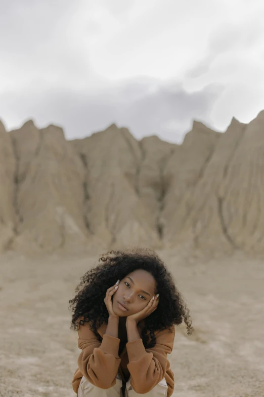 a woman sitting on a rock in the desert, an album cover, by Lily Delissa Joseph, renaissance, wavy hair spread out, 2019 trending photo, natural hair, medium format