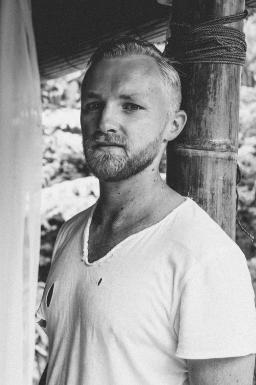 a black and white photo of a man with a beard, a black and white photo, inspired by Sigurd Swane, unsplash, fluxus, dressed in a white t shirt, no hair, small blond goatee, vacation photo