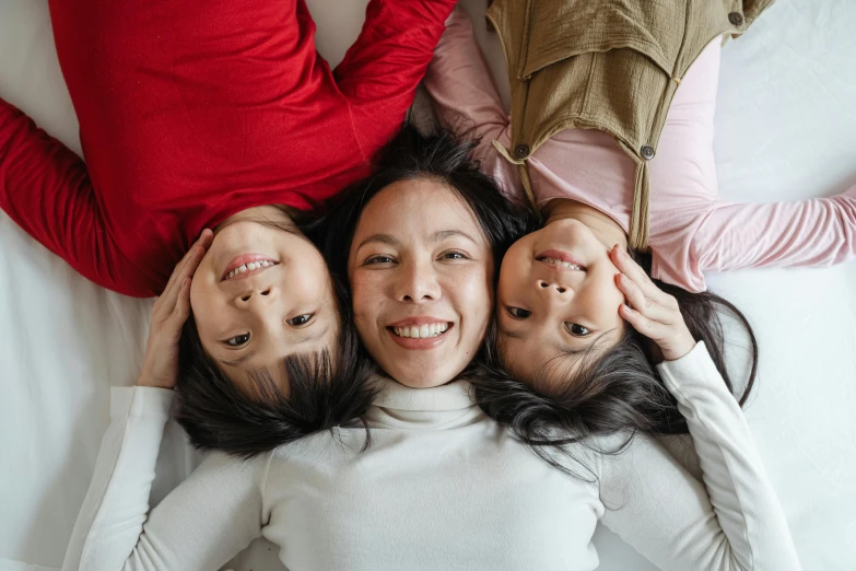 a group of women laying on top of a bed, pexels contest winner, portrait of family of three, south east asian with round face, pictured from the shoulders up, twins