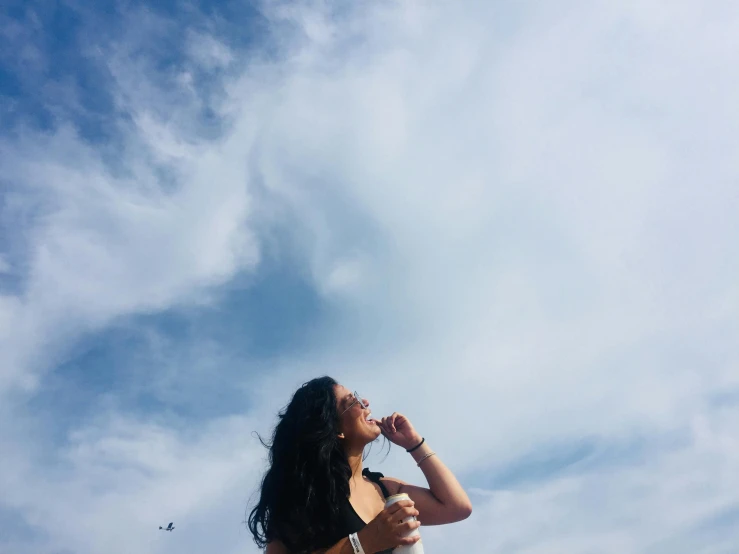 a woman standing on top of a sandy beach, pexels contest winner, happening, face looking skyward, drinking, female with long black hair, standing on a cloud