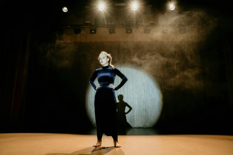 a woman in a blue dress standing on a stage, by Arabella Rankin, unsplash, light and space, masked person in corner, various posed, strong spotlights, production photo