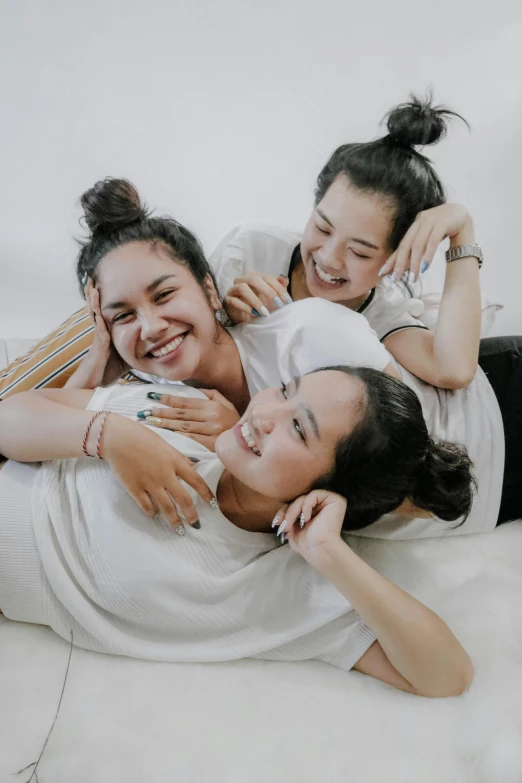 a group of women laying on top of a bed, trending on unsplash, indonesia, arm around her neck, playing, teenage
