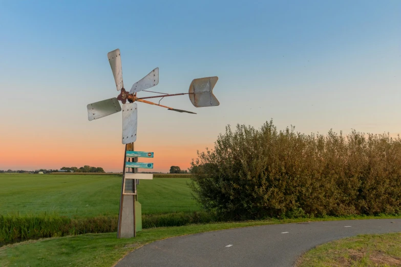 a windmill on the side of a road next to a field, by Schelte a Bolswert, pexels contest winner, kinetic art, street corner, late summer evening, outdoor art installation, at dusk!
