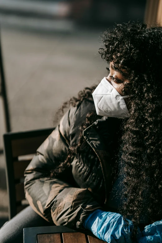 a woman sitting on a bench wearing a face mask, trending on pexels, renaissance, a black man with long curly hair, wearing jacket, head bowed slightly, disease