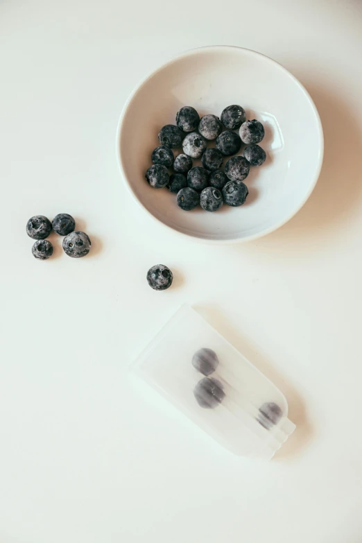 a bowl of blueberries sitting on top of a white table, a black and white photo, by Nina Hamnett, unsplash, milk cubes, silicone cover, marbled, at the counter