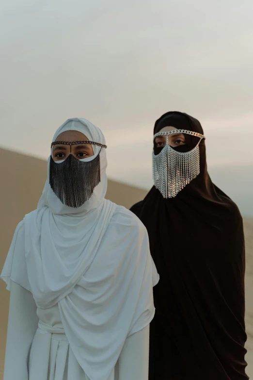 two people standing next to each other in the desert, an album cover, hurufiyya, finely masked, 2 techwear women, middle eastern style vendors, ( ( theatrical ) )