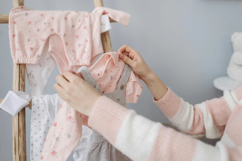 a woman hanging clothes on a clothes rack, by Alice Mason, pexels contest winner, pregnancy, pink and pink details, tiny stars, adorable design