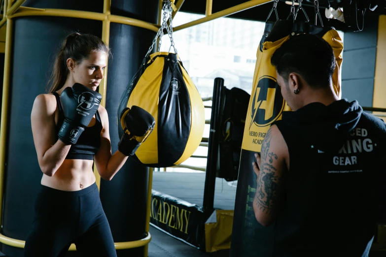 a woman standing next to a man in a boxing ring, pexels contest winner, hurufiyya, yellow and black color scheme, punching in a bag, avatar image, athletic crossfit build