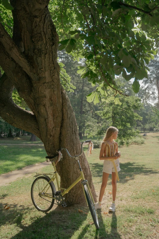 a woman standing next to a tree next to a bike, afternoon hangout, yellow