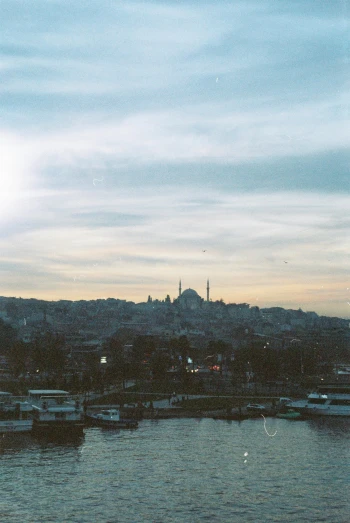 a group of boats floating on top of a body of water, a colorized photo, inspired by Elsa Bleda, pexels contest winner, hurufiyya, istanbul, black domes and spires, hills in the background, photo taken on fujifilm superia