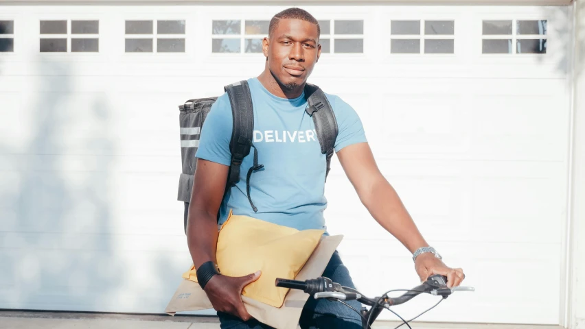 a man riding a bike in front of a garage door, dark skinned, with a backpack, delivering mail, épaule devant pose