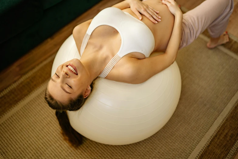 a woman laying on an exercise ball in a living room, by Aya Goda, trending on pexels, massurrealism, pregnant belly, smiling down from above, paradise garden massage, beautifully soft lit