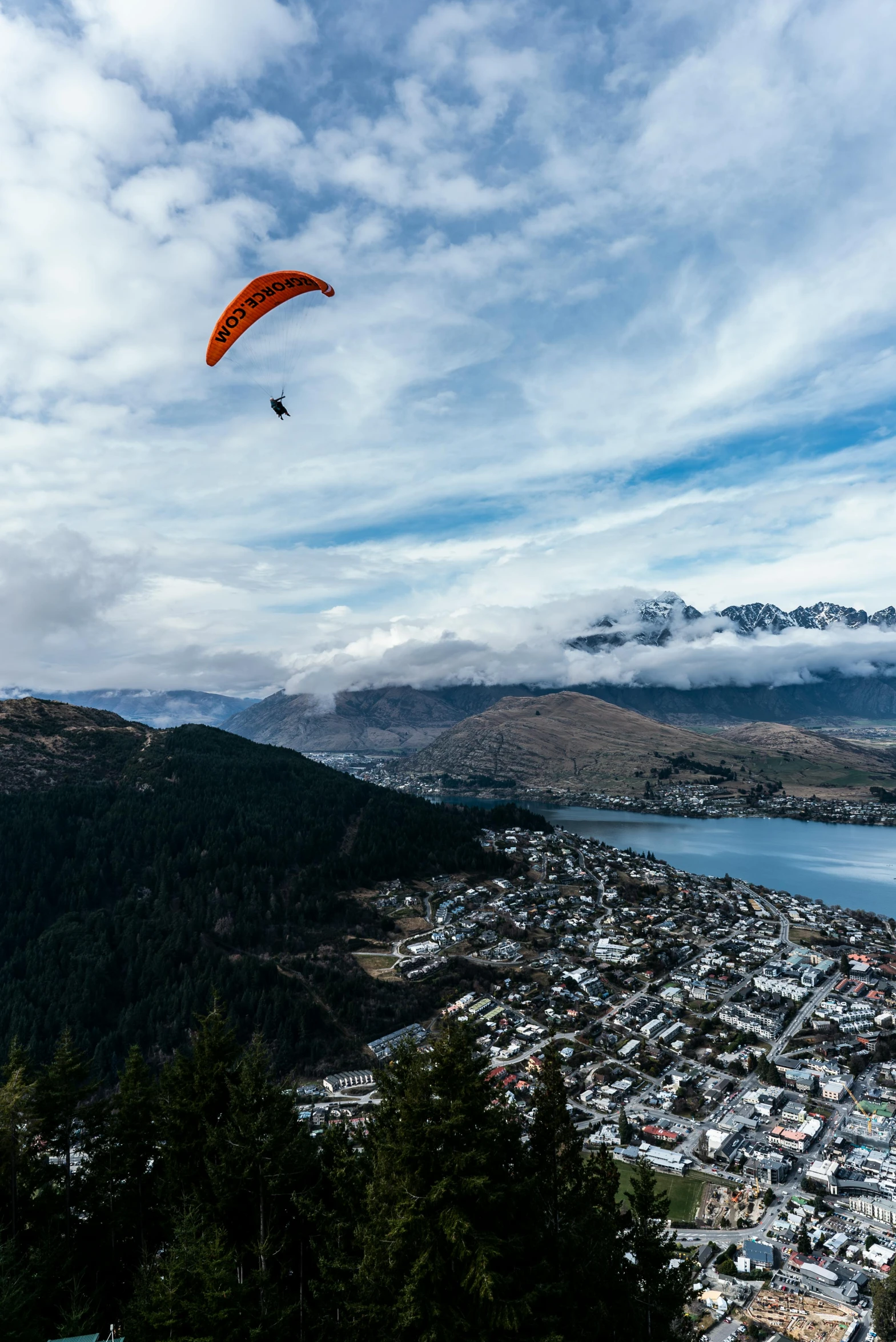 a paraglider flying over a city with mountains in the background, by Peter Churcher, hurufiyya, cloudy skies, te pae, unsplash photography, 9 9 designs