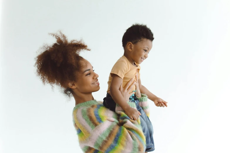 a woman holding a baby in her arms, pexels, figuration libre, wearing a colorful coogi sweater, mixed race, raising an arm, wearing a cardigan