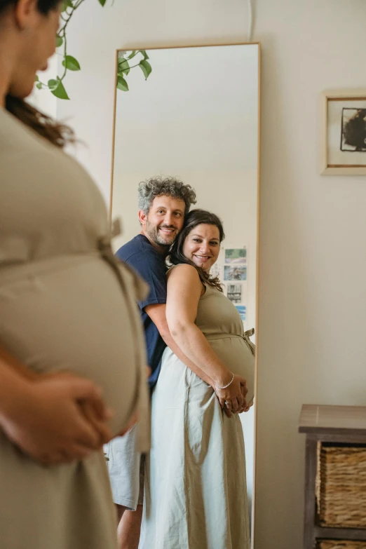 a pregnant woman standing next to a man in front of a mirror, a picture, happening, taken in 2022, profile image, australian, happy family