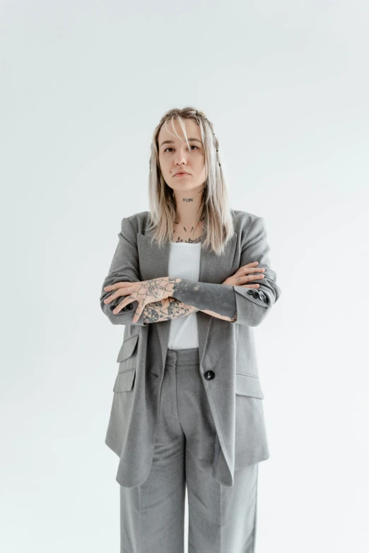 a woman standing with her arms crossed, trending on pexels, realism, grey suit, tattooed, kirsi salonen, wearing a blazer