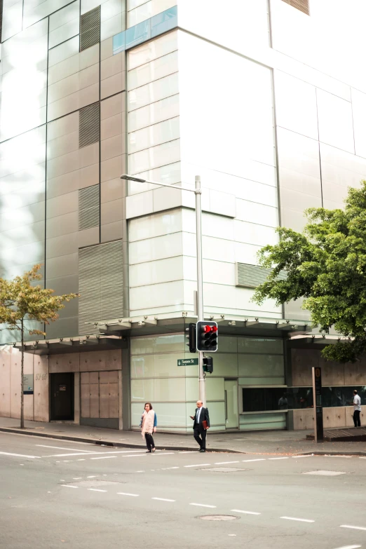 a couple of people walking across a street next to a tall building, manuka, james turrell building, street view, building facing