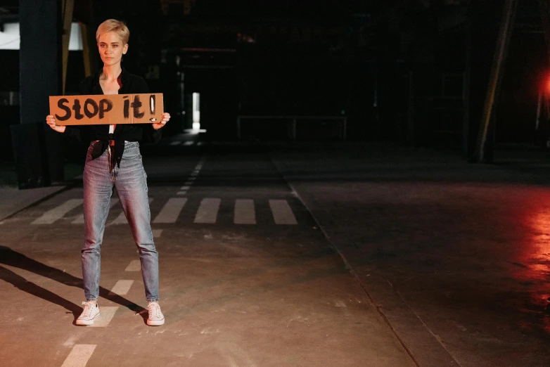 a woman holding a sign that says stop 11, by Matija Jama, pexels contest winner, elle fanning at night, full body sarcastic pose, silent hill streets, 15081959 21121991 01012000 4k