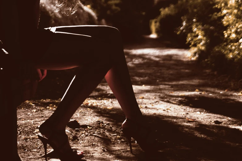 a woman in high heels sitting on a bench, inspired by Elsa Bleda, unsplash, woman in a dark forest, submissive, sepia sunshine, dark skinned
