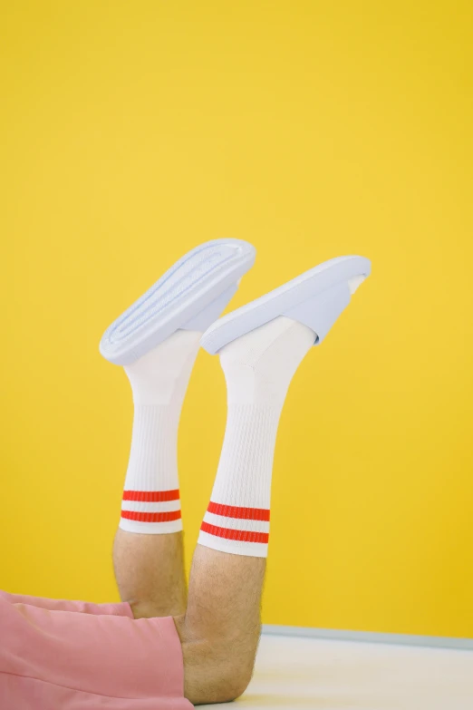 a person laying on the floor with their feet up, by Paul Bird, minimalism, wearing kneesocks, white and yellow scheme, red stripe, standing on a shelf