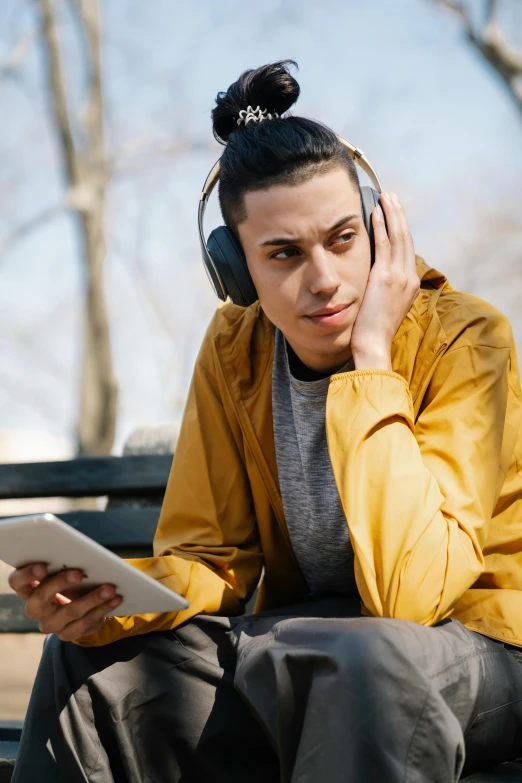 a woman sitting on a bench with headphones on, non-binary, using a magical tablet, young spanish man, trending on spotify