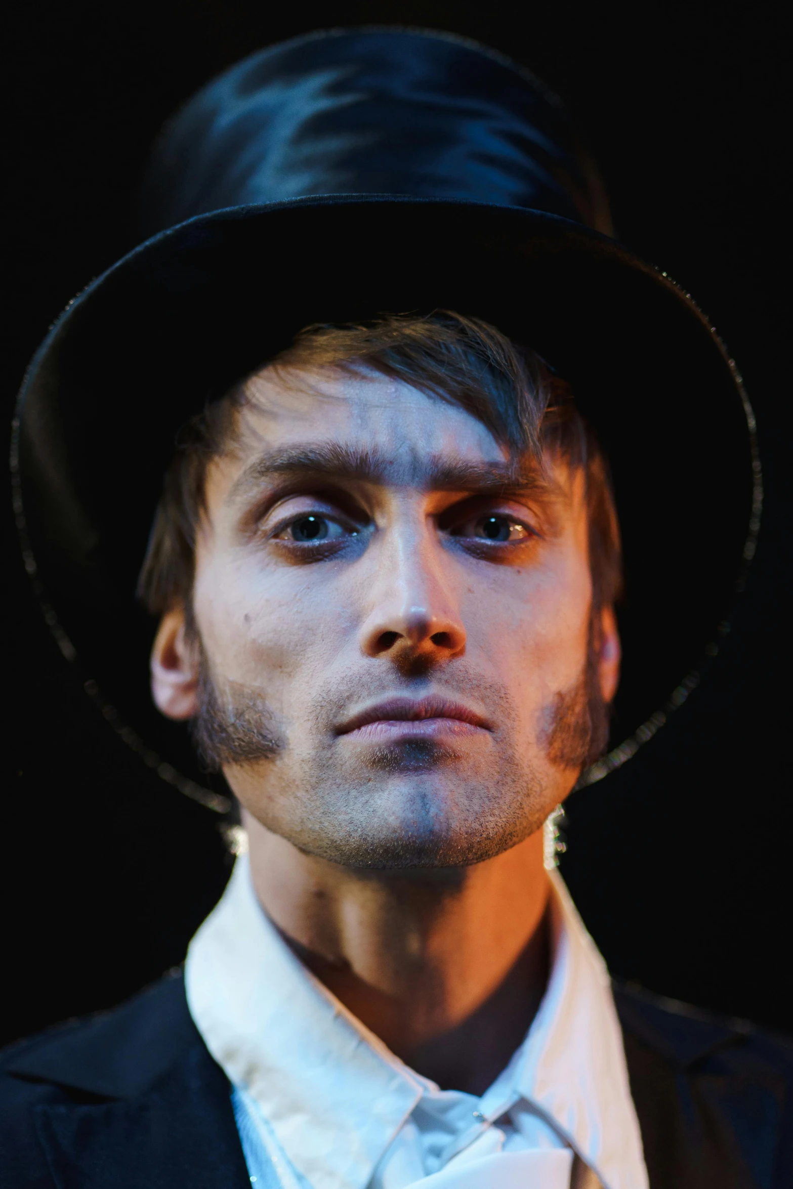 a close up of a person wearing a hat, inspired by Alexander Kanoldt, sideburns, spotlight in middle of face, skinny male magician, lgbtq