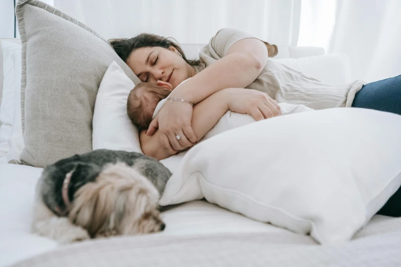 a woman laying on top of a bed next to a dog, by Emma Andijewska, pexels contest winner, symbolism, babies in her lap, australian, husband wife and son, 1 5 0 4