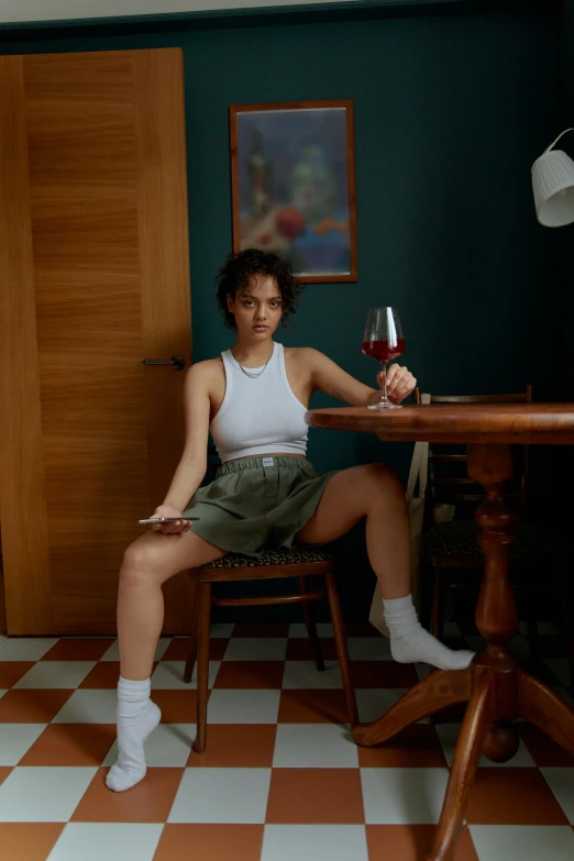 a woman sitting at a table with a glass of wine, a portrait, inspired by Nan Goldin, pexels contest winner, renaissance, bra and shorts streetwear, nathalie emmanuel, portrait full body, marat zakirov