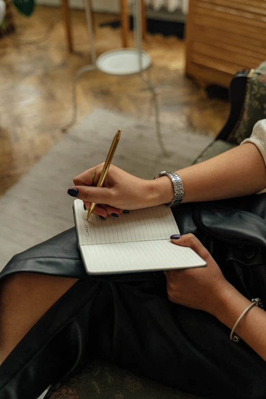 a woman sitting on a couch writing in a notebook, inspired by Ruth Jên, leather jewelry, curated collections, high quality upload, multiple stories