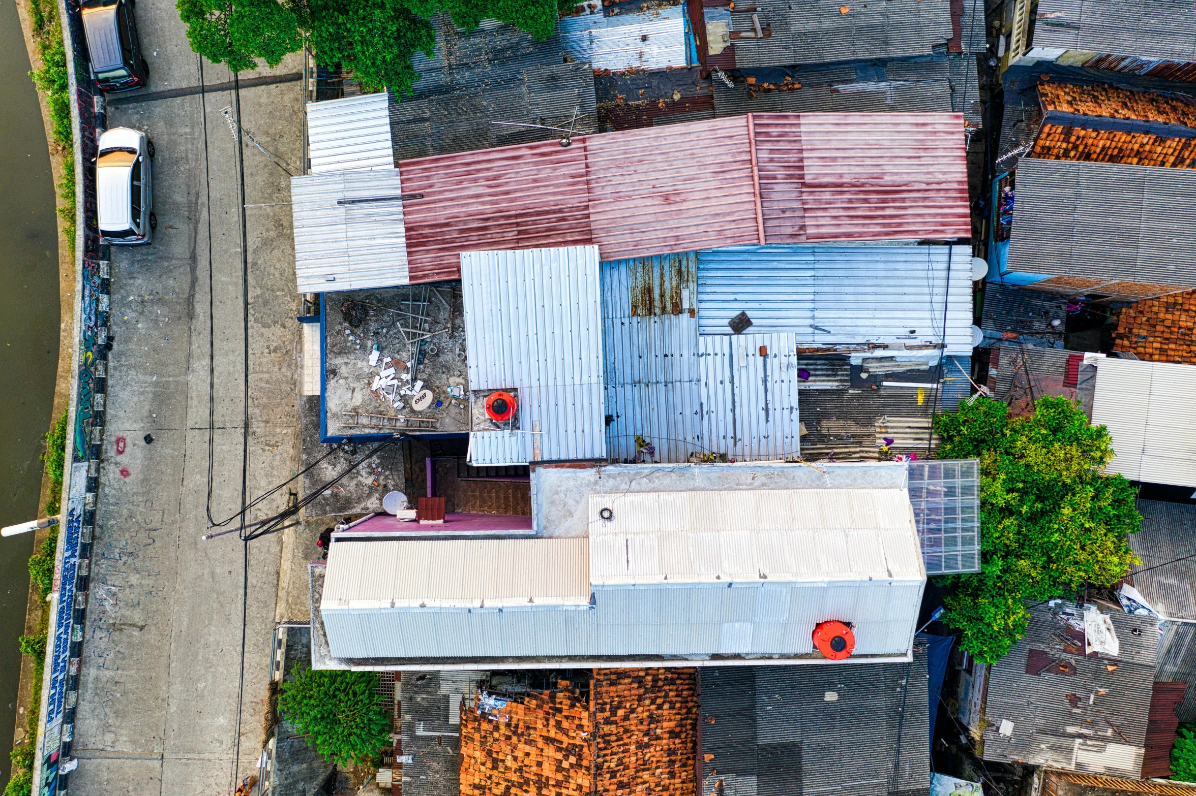 a bird's eye view of a building next to a body of water, pexels contest winner, photorealism, scrapyard architecture, hiding in the rooftops, galvalume metal roofing, red - yellow - blue building