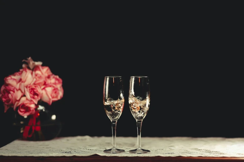 a couple of wine glasses sitting on top of a table, a still life, inspired by Elsa Bleda, pexels, romanticism, exploding roses, champagne, grainy quality, medium long shot