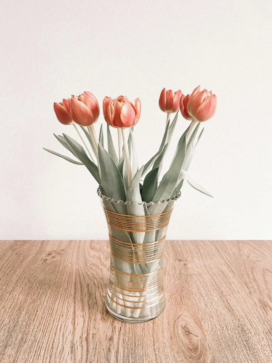 a vase filled with pink flowers on top of a wooden table, a colorized photo, by Andrée Ruellan, unsplash, orange ribbons, tulip, 🎀 🗡 🍓 🧚, wrapped in wires and piones